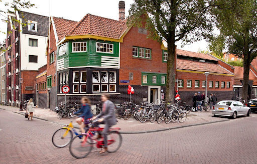 Splendor Amsterdam venue exterior with brick architecture and green shutters on Amsterdam street corner with cyclists.