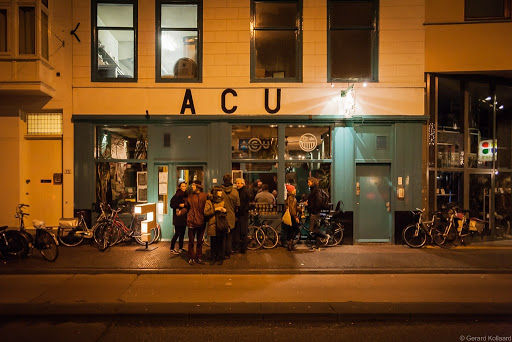 ACU live music venue storefront at night with illuminated interior, bikes outside, and crowd gathered for performance.