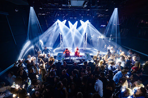 Patronaat concert hall with performers on stage, dramatic blue lighting rig, and crowd of standing audience members.