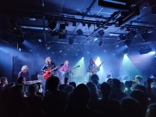 EKKO live music venue with band performing on stage under blue stage lighting, crowd of audience members in foreground.
