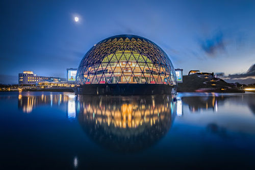 AFAS Theater illuminated geodesic dome venue reflected in water at dusk, with stage lighting and architectural framework for live performances.