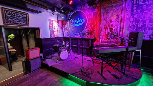 Muziekcafé Pitchers stage with purple neon lighting, drum kit, PA system, and audience seating area for live music performances.