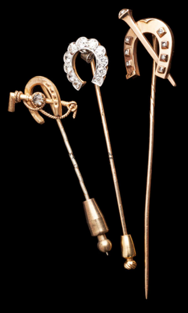 A trio of gold & diamond stick pins with horse shoe designs, with one crossed by a riding crop, an a...