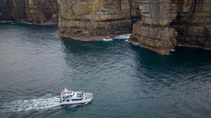 Tourist boat cruising along enormous coastal cliffs