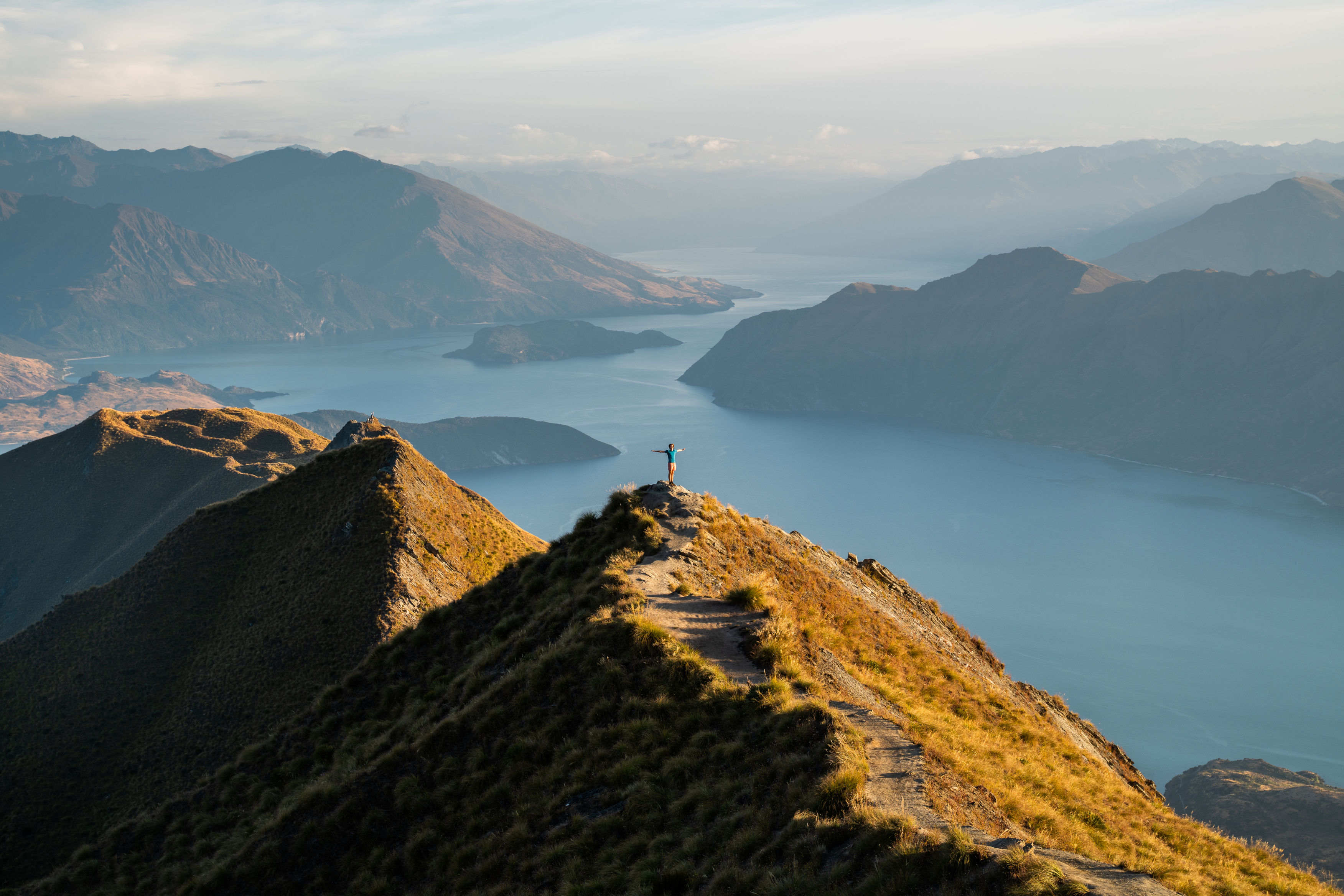 Hiker standing atop of mountain with massive lake in the background