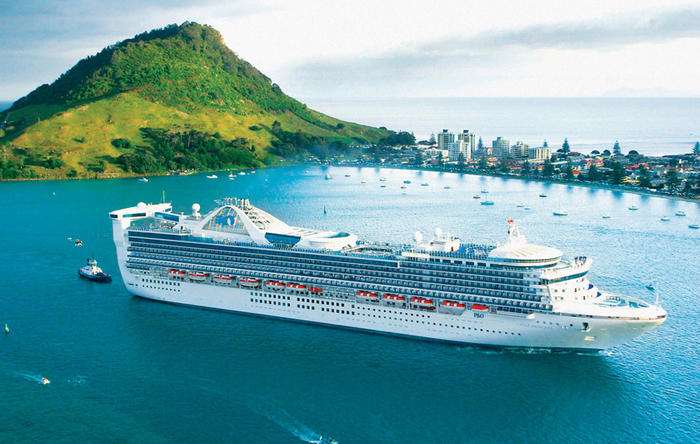 aerial view of a large cruiseship in the bay with a coastal city in the background