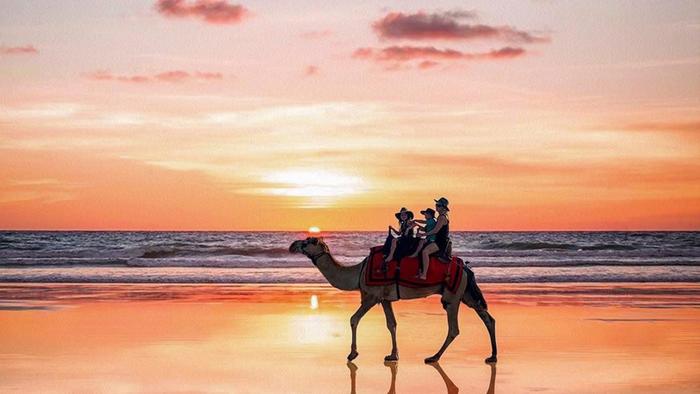 People on a camel with a calm sunset in the background at Cable Beach