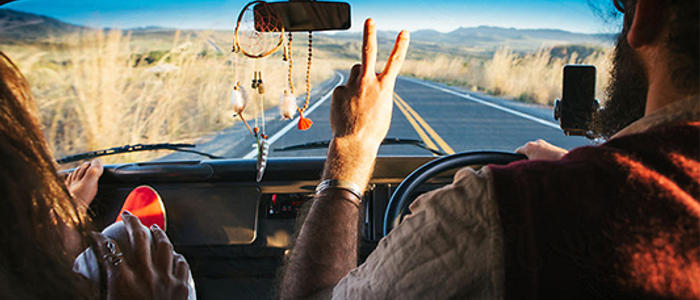 Hippy couple giving the peace sign in a rental campervan