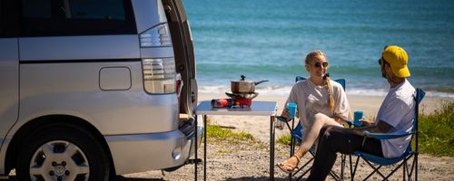 People relax for a meal behind a campervan