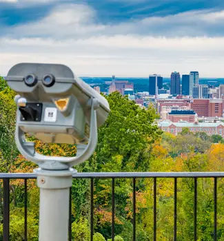 Fall colors from leaves framing the city scape of Birmingham, Alabama with a telescope in the foreground.