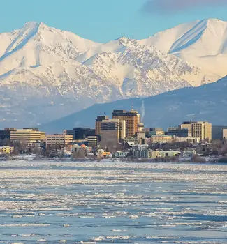 Anchorage, Alaska waterfront with city buildings and snowy mountains in the background.