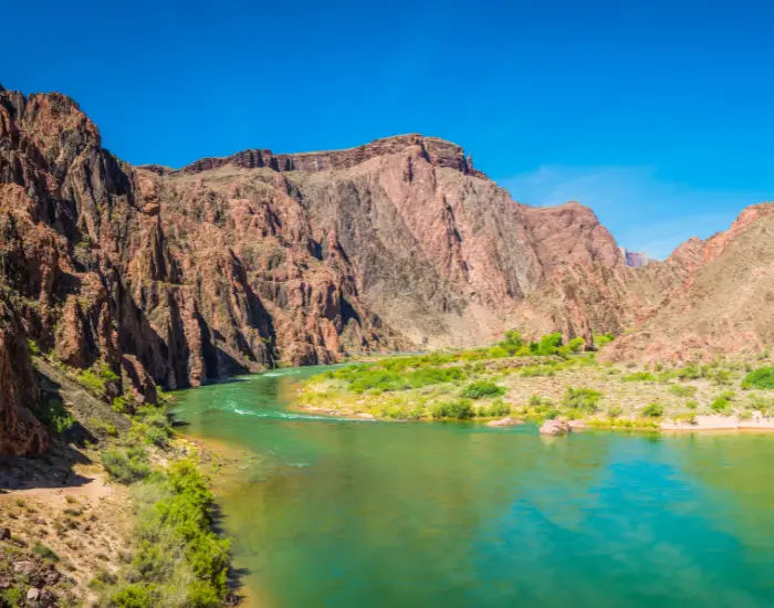 Colorado River flowing down the Phantom Ranch area in Arizona with turquoise green waters and high red mountains.