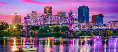 Colorful Little Rock city skyline of Arkansas with a small boat riding over the walk river waters and bridges stretching over to the city.