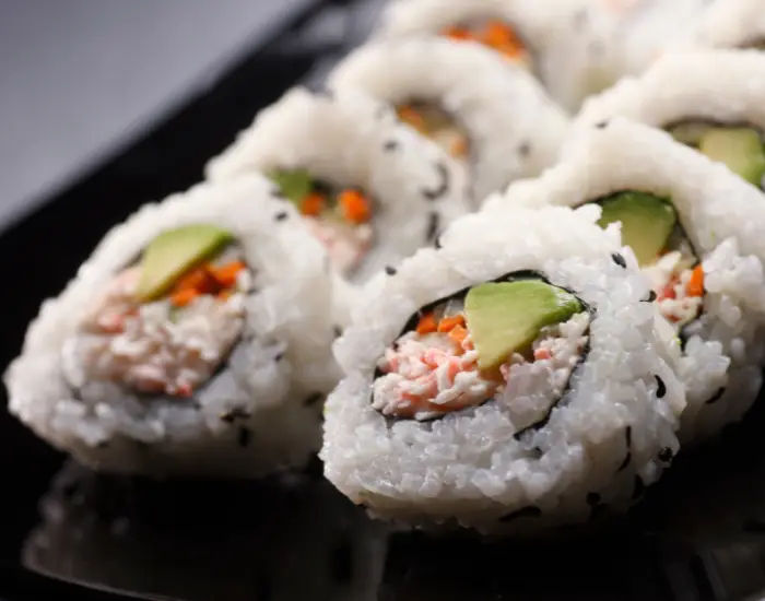 Close up of California sushi rolls with imitation crab, mayo, avocado, cucumbers, rice, seaweed, and sesame seeds.