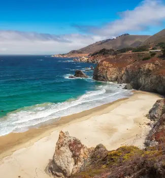 California Beach Big Sur coastline in the Pacific Ocean with mountains and deep blue waters on a sunny partly cloudy day.