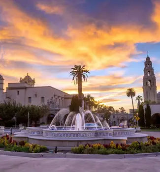 San Diego's Balboa park at twilight with a water fountain in the middle, cathedral, and palm trees.