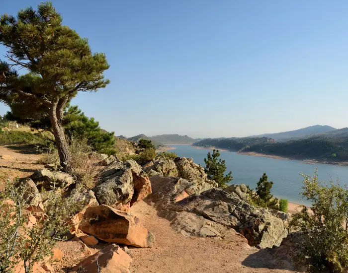 Rocky biking trails of Horsetooth Reservoir right outside of Fort Collins, Colorado on a sunny day with red rocks, trees, and a body of water.