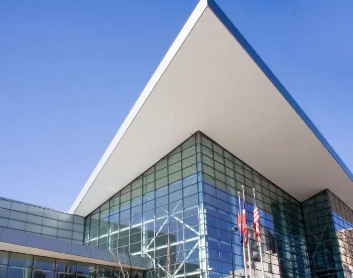 Corner view of the Colorado Convention Center during the day built with reflective glass panels and flags flying out front.