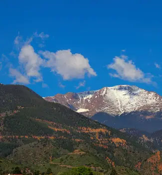 Pikes Peak in the rocky mountains as seen from Colorado Springs with one tree and greenery field mound with another covered in snow.