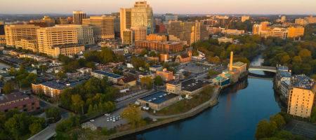 Sunrise aerial city view of Wilmington, Delaware skyline with a river running between buildings and natural trees spread throughout the land.