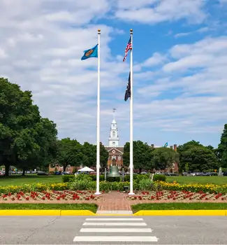 Capital Building in the distance surrounded by trees, nature, and flowers with flags raised in Dover, Delaware.
