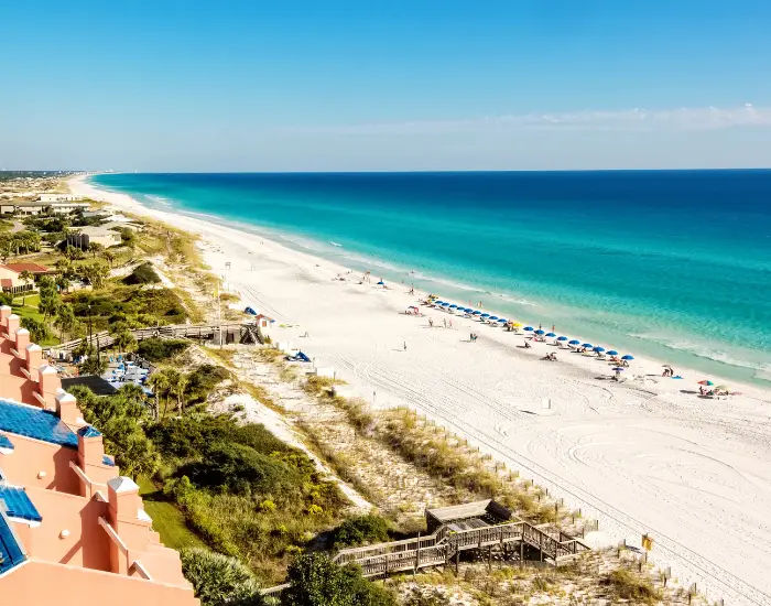 Long stretch of Miramar Beach in Destin, Florida showing the green and blue waters from the Gulf of Mexico and flat landscape.