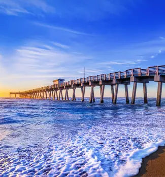 Sunrise view of the Straits of Florida with ocean waves creeping up the wet beach sands and a raised walking dock.