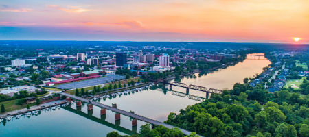 Downtown Augusta, Georgia state overview of two bridge, a body of water, buildings, and dense green trees and sunrise.