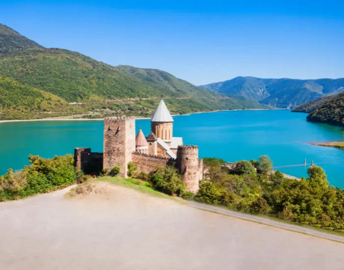 Ananuri castle in Georgia alongside Aragvi river from a high point on a sunny day with trees.