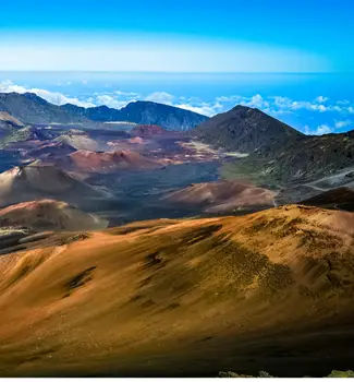 Haleakala crater in Maui Hawaii from an aerial view with clouds, mountain, rocks, and a vivid blue sky at day time.