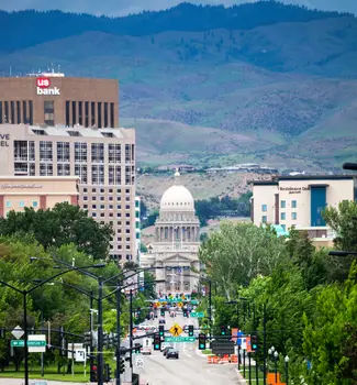 Downtown Boise, Idaho city street leaving down towards the state capitol building lined with green trees with a mountain background.