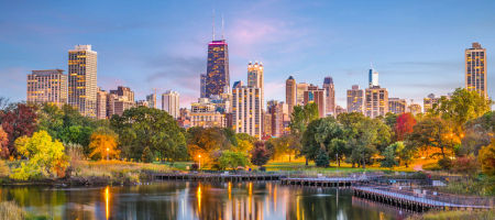 Lincoln Park, Chicago, Illinois city skyline view with a lake in the foreground and lit up buildings in the background on a partly clear day.