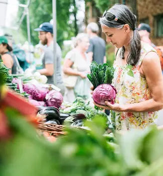 Female travel nurse holding purple cabbage looking at produce at an Illinois Fox River farmer's market.