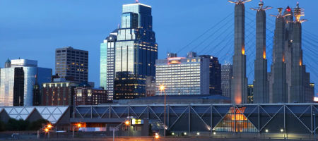 Kansas City skyline at twilight with reflective glass buildings, highways, and bridges lit up.