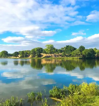 Trees and natural greenery reflecting off Overland Park Lake in Kansas on a sunny partly cloudy day.