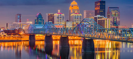 Louisville, Kentucky city skyline and waterfront at night with a bridge stretching over Ohio river.