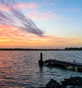 Sunrise in Bayou, Louisiana from the shores of a beach with silhouettes of land and the dock.