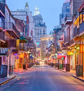 Bourbon Street in New Orleans, Louisiana at twilight with lit up shopping stores and restaurants down a road.