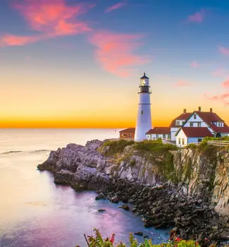 Cape Elizabeth, Maine at Portland Head Light showing a lighthouse at the end of an island surrounded by water at dusk.