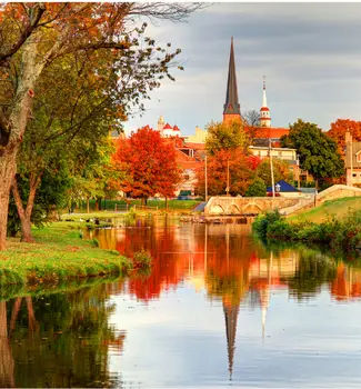 Frederick, Maryland buildings peeking over autumn colored red trees reflecting off a calm pond.