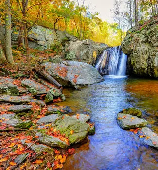 Kilgore Falls natural environment in Maryland in autumn with colorful leaves draped on top of large rock slates in a forest.