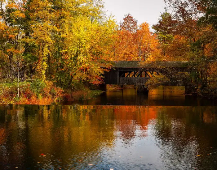 River under an old wooden bridge in an autumn forest filled with yellow and red trees located in Massachusetts.