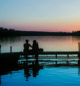 Travel nurse couple silhouette sitting on a dock during sunrise in lake Chargoggagoggmanchauggagoggchaubunagungamaugg, Massachusetts.