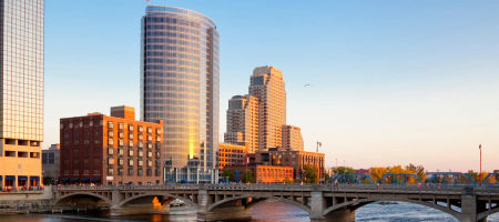 View of a city in Michigan with glass buildings and a bridge crossing over a large body of water during golden hour.