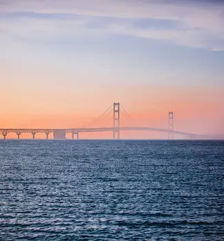 The Straits of Mackinac under the bridge of Mackinac in Michigan during a foggy morning with warm colors.