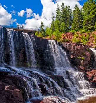 Gooseberry Falls on Minnesota's North Shore Drive streaming into a lake surrounded by rocky mountains and green pine trees.