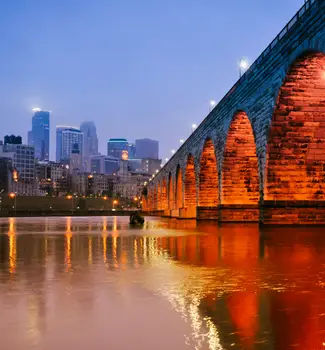 Minneapolis Rivers under an arched brick bridge leading into the Minnesota city at night with lights reflecting off the water.