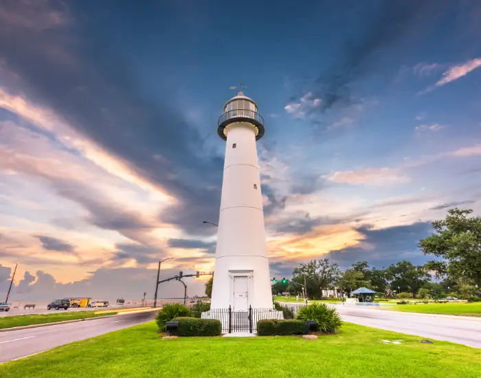 Biloxi Lighthouse in Mississippi on top of vivid green grass surrounded by streets on a cloudy day.