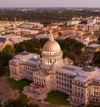 Aerial view of the Jackson Capital State Building in Mississippi at dusk surrounded by other city buildings and green trees.