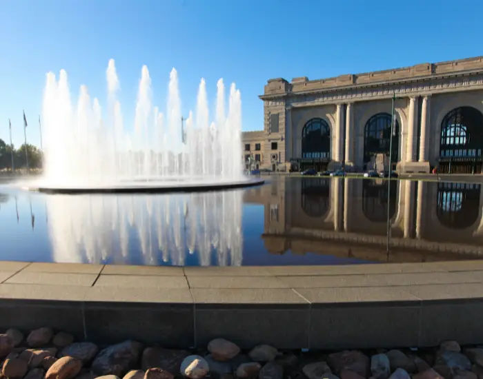 Fountain shooting water in the air between calm waters reflecting buildings outside of Kansas City Union Station in Missouri.